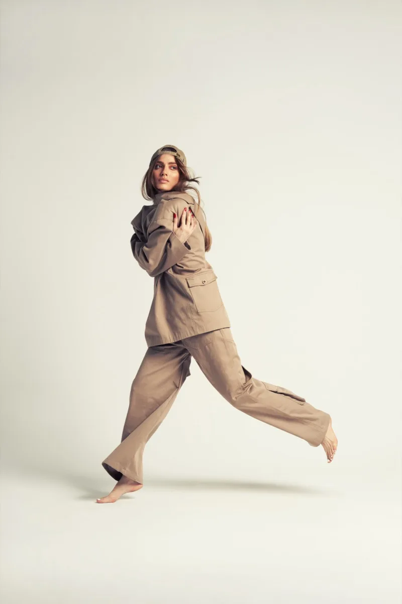 Woman in a beige suit mid-stride against a light backdrop
