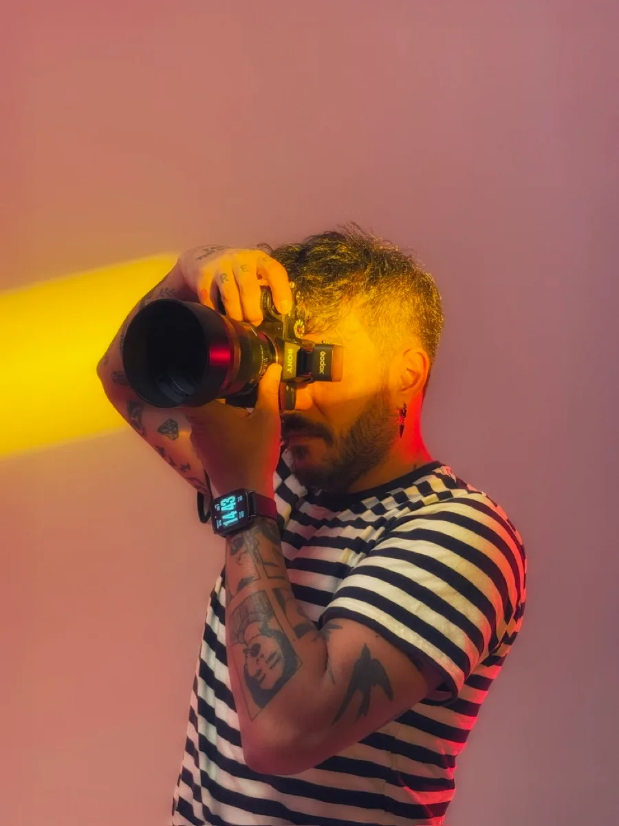 Çağlar Doğan beim Fotografieren, die Kamera am Auge, gelbes Licht auf rosa Hintergrund